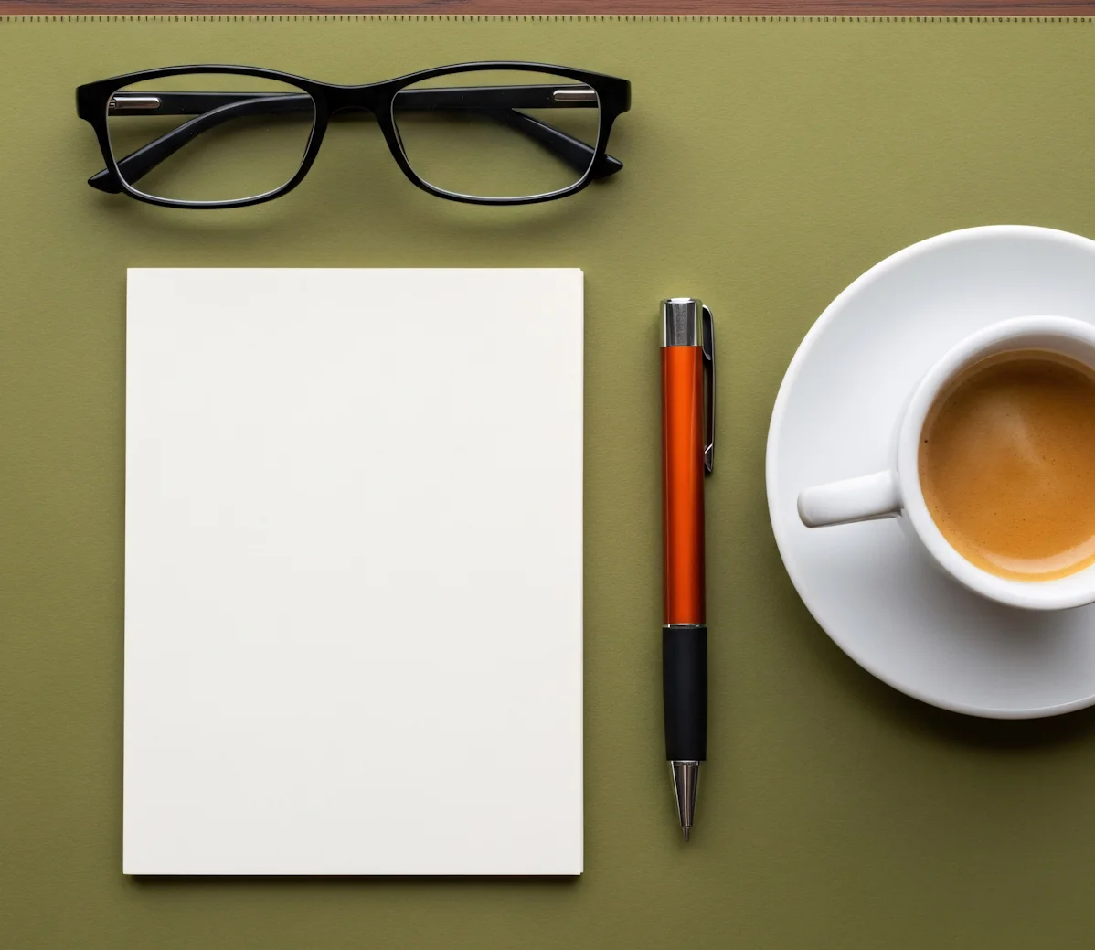 Weiße leere Notizkarte neben schwarzer Brille, orange-schwarzem Kugelschreiber und Tasse Espresso.